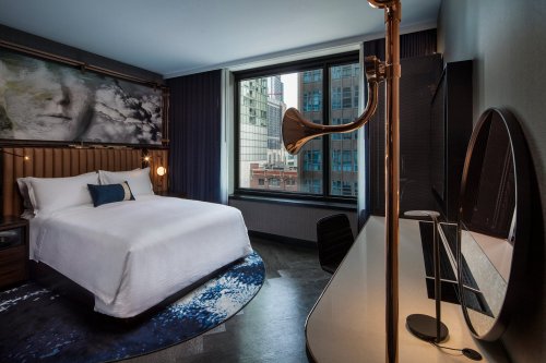 Modern hotel room featuring a queen bed, large window, stylish decor, and a unique floor lamp.