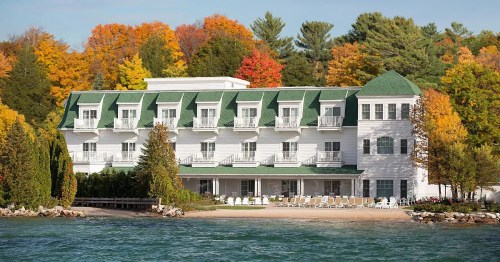 A charming white hotel with green roofs, surrounded by colorful autumn trees and a serene waterfront.