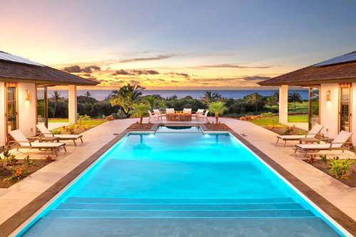 A luxurious poolside view at sunset, surrounded by palm trees and elegant lounge chairs.