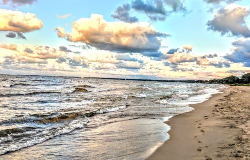 A serene beach scene with gentle waves, sandy shore, and a colorful sky filled with clouds at sunset.