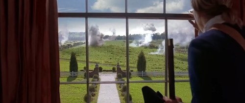 A person looks out a window at a grassy landscape with smoke rising, suggesting a distant conflict or battle.