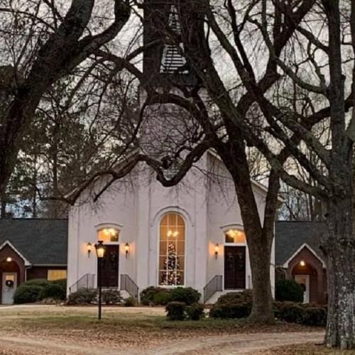 A charming church surrounded by bare trees, with warm lights glowing in the windows during twilight.