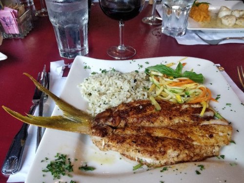 A plate of seasoned fish fillets with rice and mixed vegetables, accompanied by a glass of red wine.