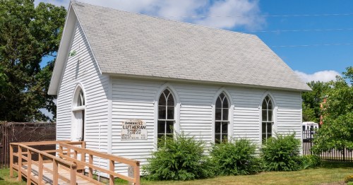 The small, white clapboard Immanuel Lutheran Church building features gothic-arched windows and a wooden ramp, preserving the history of Carlos, Minnesota, near Alexandria.