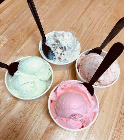 Four bowls of ice cream in various flavors: green, pink, white with chocolate, and light pink, each with a spoon.