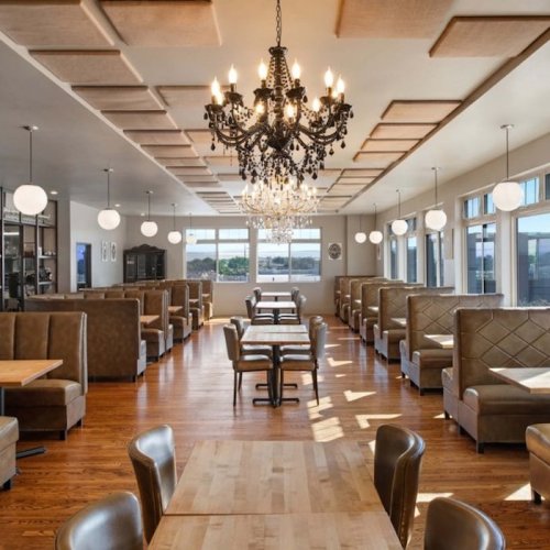 A modern restaurant interior featuring elegant seating, a chandelier, and large windows with a scenic view.