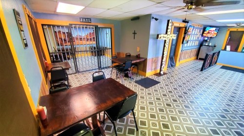 Interior of a restaurant with tables, a jail-themed decor, and a counter with a menu display.