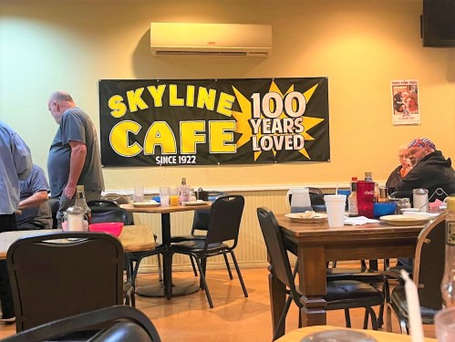 Interior of Skyline Cafe with a banner celebrating 100 years, featuring diners at tables and a warm atmosphere.