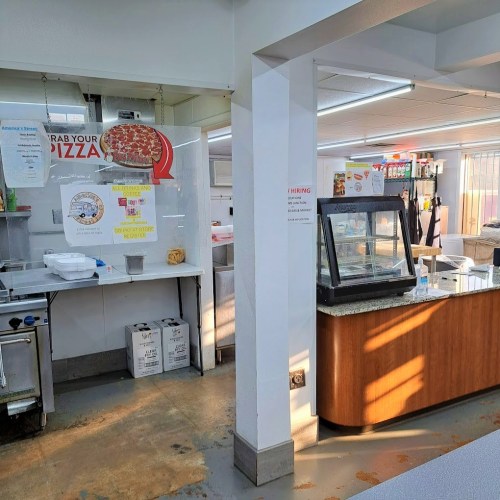 Interior of a pizza shop with a counter, display case, and various kitchen equipment. Brightly lit and clean environment.