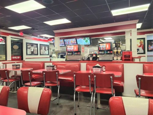 A retro diner interior with red booths, a counter, and menu screens, featuring a classic fast-food vibe.