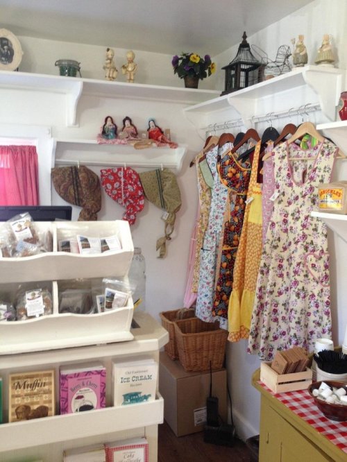 A cozy shop interior featuring colorful dresses on hangers, vintage decor, and a display of baked goods.