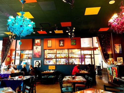 Colorful restaurant interior with artistic decor, vibrant chandeliers, and patrons dining at tables.