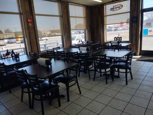 Interior of a restaurant with empty tables and chairs, large windows letting in natural light.