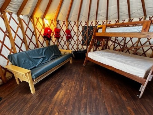 Interior of a yurt featuring a wooden bunk bed, a sofa, and wooden walls with a warm, inviting atmosphere.