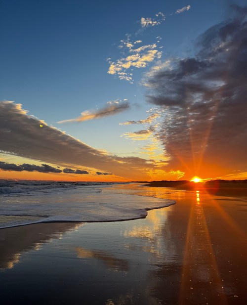 A stunning sunset over a beach, with vibrant colors reflecting on the wet sand and gentle waves lapping at the shore.