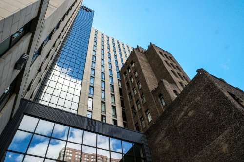 A view of tall buildings from below, showcasing a mix of modern glass and historic brick architecture against a blue sky.