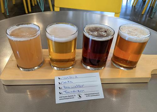 Four glasses of beer in a flight, with a tasting card listing the names of each brew.