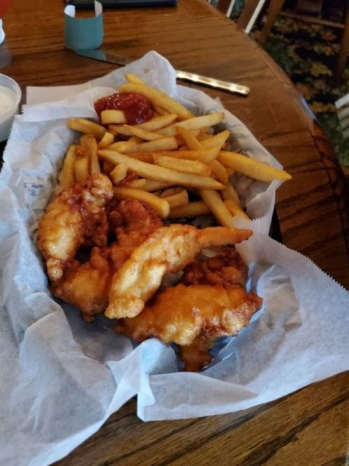 A plate of crispy fried chicken tenders with a side of golden French fries and dipping sauce.