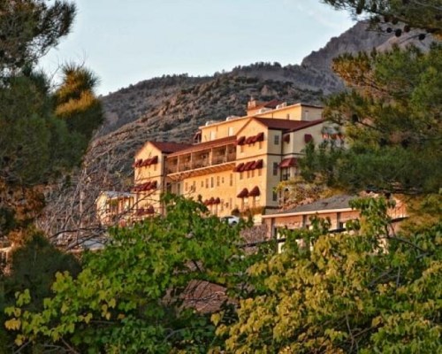 A hillside hotel surrounded by trees, with mountains in the background and a warm sunset glow.