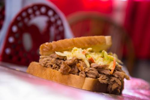 A close-up of a pulled pork sandwich with coleslaw on two slices of bread, set against a blurred background.