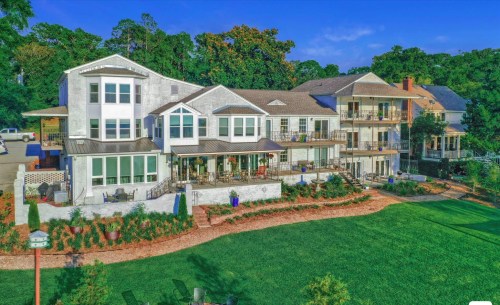 A large, modern house with multiple balconies surrounded by greenery and a well-maintained lawn.