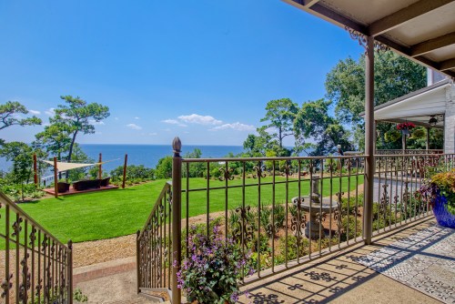 A scenic view of a lush garden leading to the ocean, framed by a decorative railing and bright blue sky.