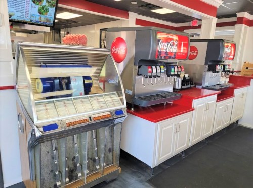 A vintage jukebox next to modern Coca-Cola drink dispensers in a bright, casual dining area.
