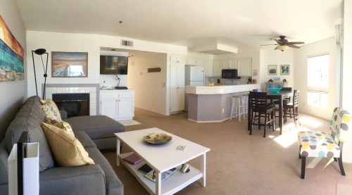 Bright, modern living room with a gray sofa, coffee table, dining area, and kitchen in an open layout.