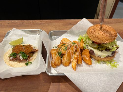 A plate with a taco topped with sauce and lime, alongside a burger with toppings and a side of golden fries.