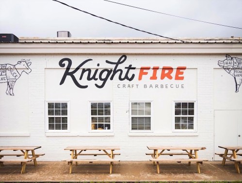 Exterior of KnightFIRE Craft Barbecue with a mural and picnic tables in front.