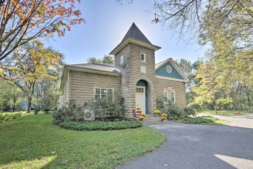 A charming stone house with a tower, surrounded by greenery and colorful flowers in a serene outdoor setting.