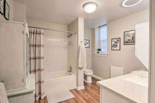 Bright bathroom featuring a tub, shower, toilet, and modern decor with wooden flooring and framed artwork on the walls.