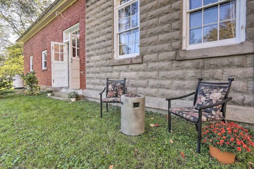 Two chairs with floral cushions sit beside a small table on a grassy area next to a brick building with large windows.
