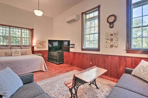 Cozy room with a bed, sofa, wooden accents, and large windows, featuring a clock and decorative wall art.