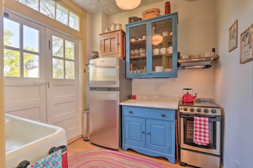 A cozy kitchen featuring a blue cabinet, stainless steel appliances, and a colorful braided rug on the wooden floor.