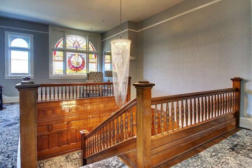 A wooden staircase with a decorative railing, featuring a stained glass window and a modern chandelier above.