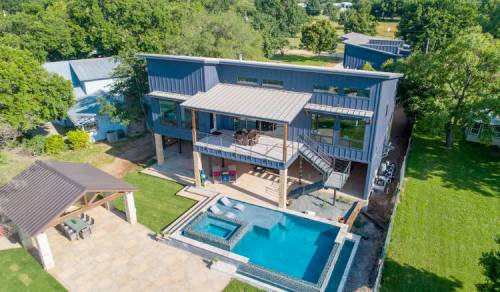 Aerial view of a modern house with a pool, patio, and landscaped yard surrounded by trees.