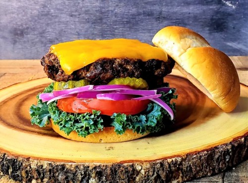 A delicious cheeseburger with a beef patty, cheddar cheese, lettuce, tomato, pickles, and red onion on a wooden platter.