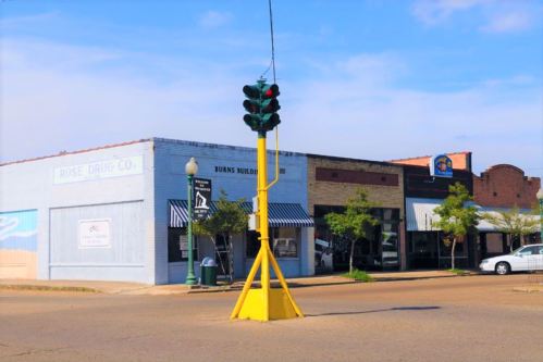 A street view featuring colorful buildings, a traffic light, and trees along the sidewalk on a sunny day.