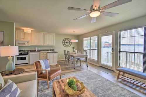 Cozy living area with a kitchen, dining table, and large windows overlooking a lake. Modern decor and natural light.