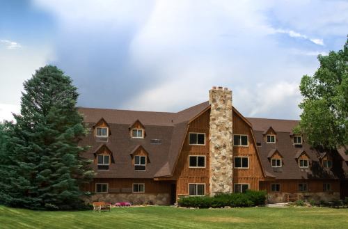 A large wooden lodge with a stone chimney, surrounded by trees and a grassy area under a cloudy sky.