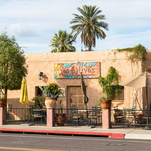 Exterior of a Mexican restaurant with a colorful sign, palm trees, and outdoor seating under umbrellas.