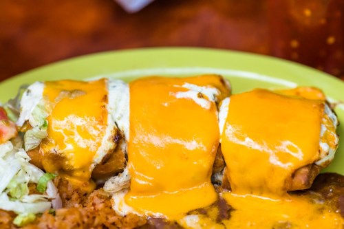 A close-up of a plate featuring three enchiladas topped with melted cheese, served with rice and lettuce.