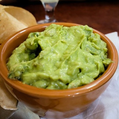 A bowl of creamy guacamole served with tortilla chips on the side.