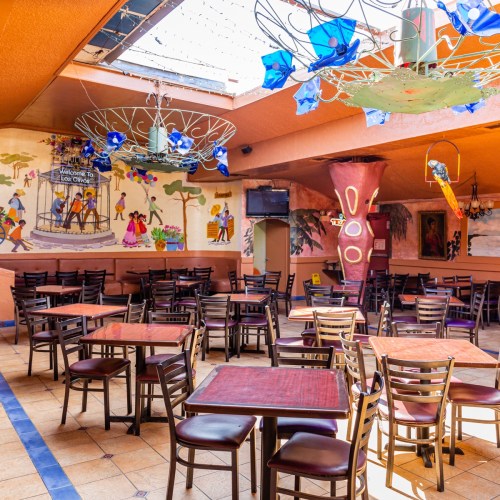 Colorful restaurant interior with empty tables, vibrant murals, and decorative lighting fixtures.