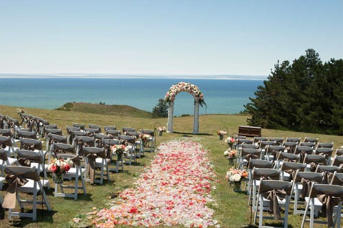 A scenic outdoor wedding setup with chairs, floral decorations, and an arch overlooking the ocean.