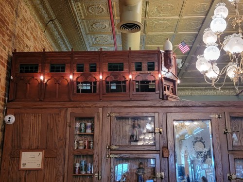 A wooden model of a building with lights, displayed on top of a cabinet in a vintage-style interior.