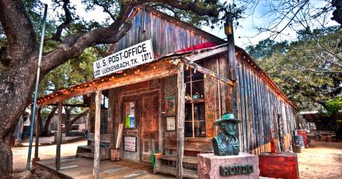 Historic U.S. Post Office in Luckenbach, Texas, featuring rustic wooden architecture and a statue in front.