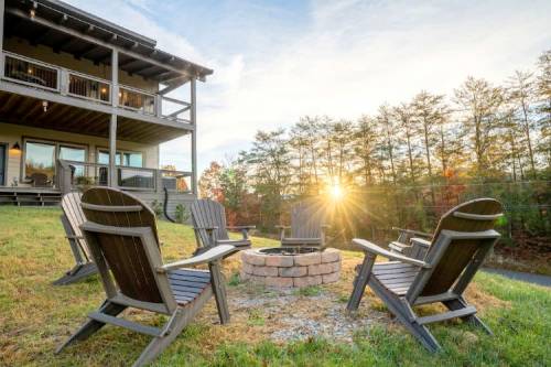 A cozy outdoor fire pit surrounded by wooden chairs, with a house and trees in the background at sunset.