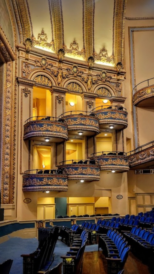 Interior of a grand theater featuring ornate balconies, golden details, and blue seating in a historic setting.